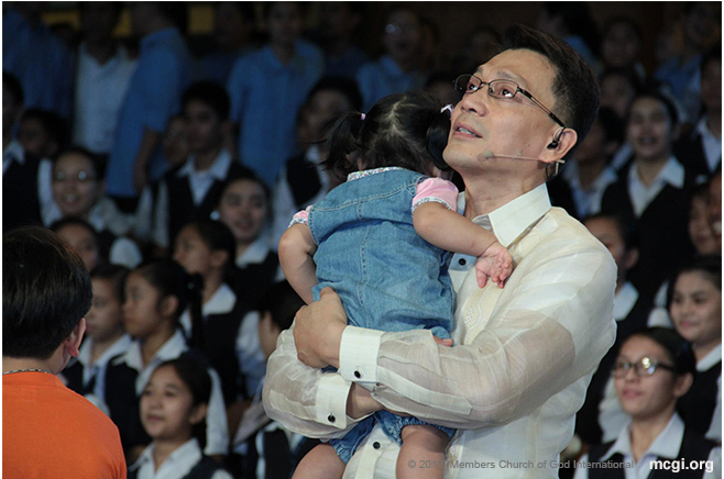 Looking at the big LED screen on stage, Bro. Daniel Razon carries his daughter as the whole congregation offers a song of praise to God.